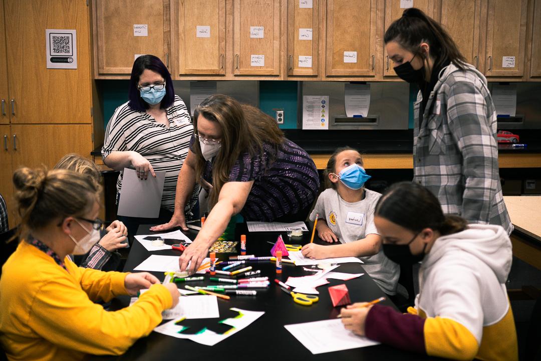 四个中学女生正在制作金字塔形状的纸模型, cubes and dodecahedrons with the help of Dr. Margaret Watts and Dr. Barbara Jennings Herzog, who teach math at 十大网络娱乐平台注册, 和Bailee back, 初级基础教育和特殊教育专业. 他们在十大网络娱乐平台注册科学大楼的一间教室里. 